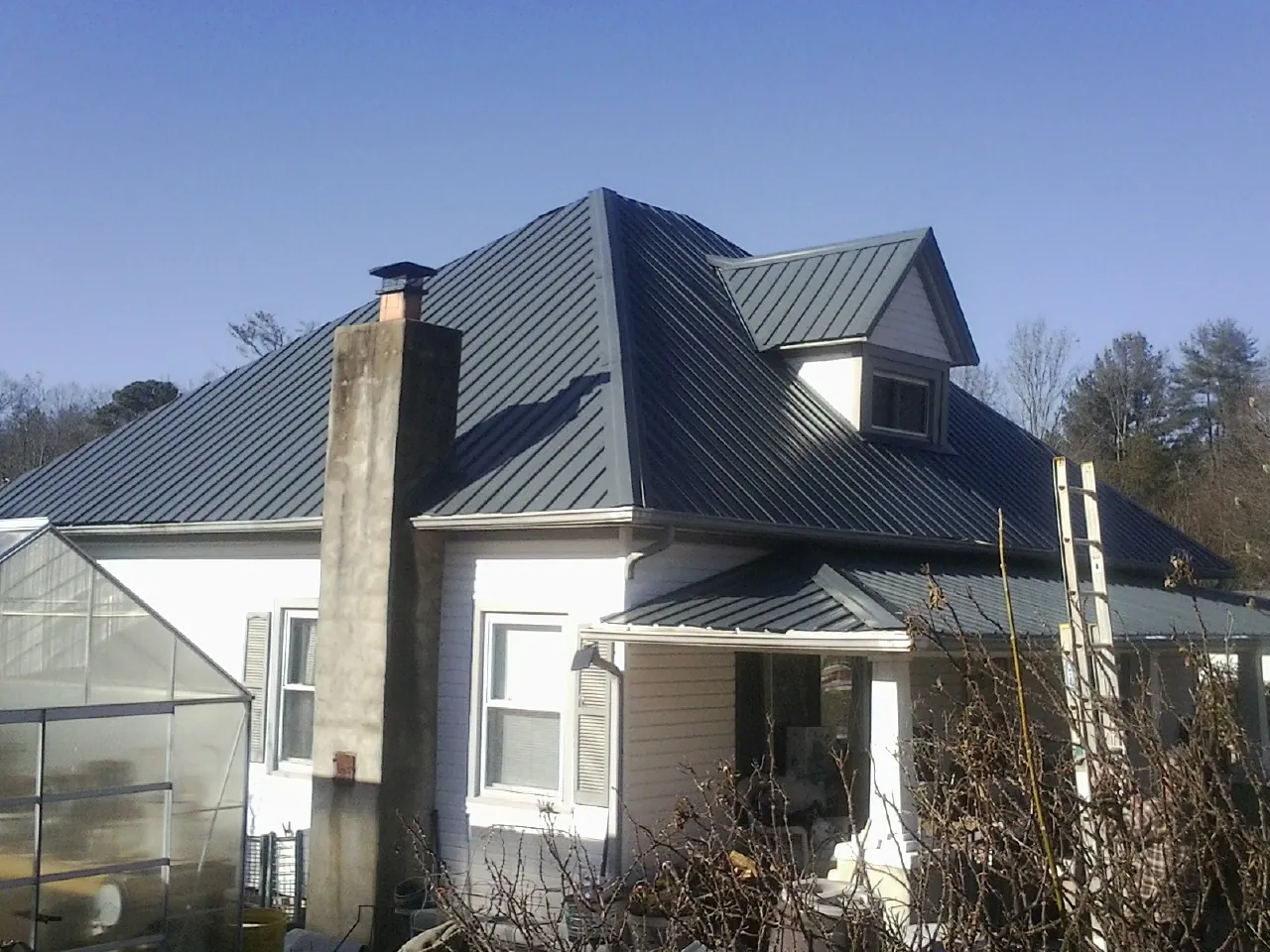 Dark blue standing seam metal roof on a white farmhouse with dormer — Slate & Tile Roof Repair by Roofing Brothers in Sevier