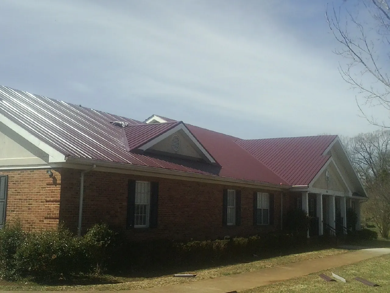 Red metal roof with gabled entries on a long brick building, from a Hail Damage Roof Repair job in Sevier