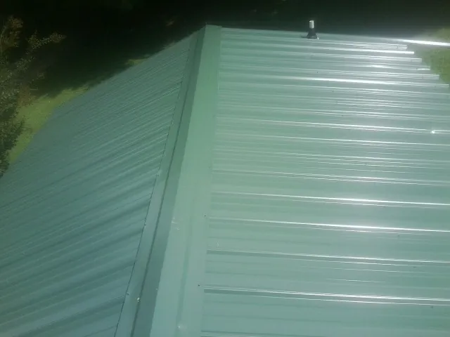 New green metal panels meeting at the ridge of a roof — Flat Roof Repair work by our crew in Sevier