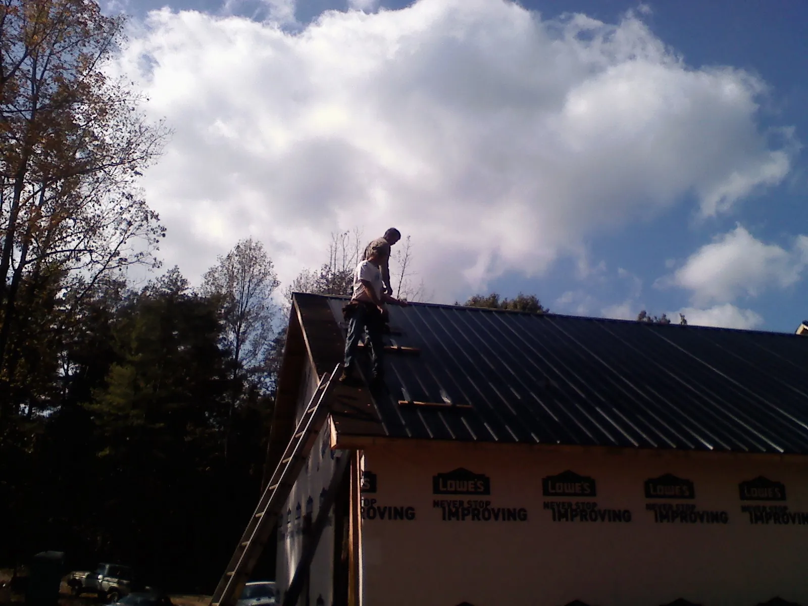 Roofer fastening dark metal panels high against a cloudy sky, from a Roof Inspection job in Sevier