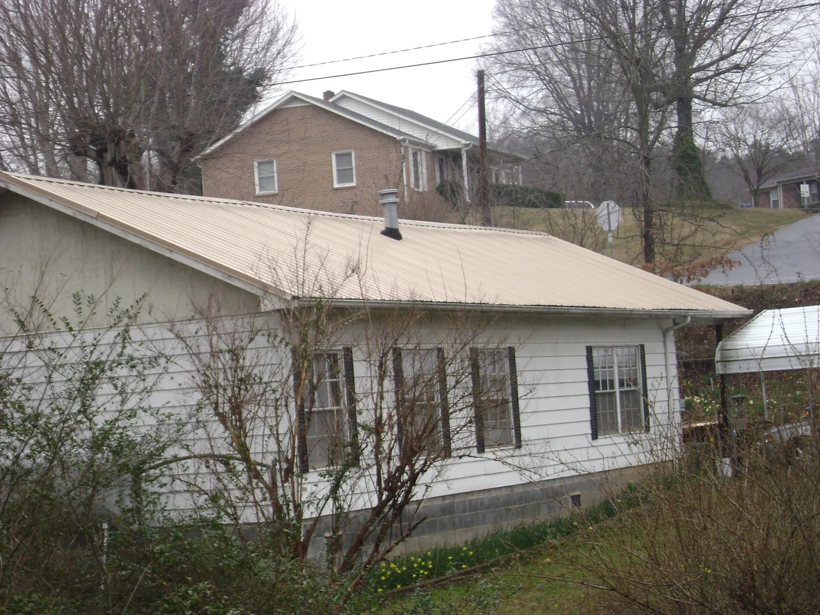 Tan metal roof on a white sided house set into a hillside — Commercial Roofing by Roofing Brothers in Sevier