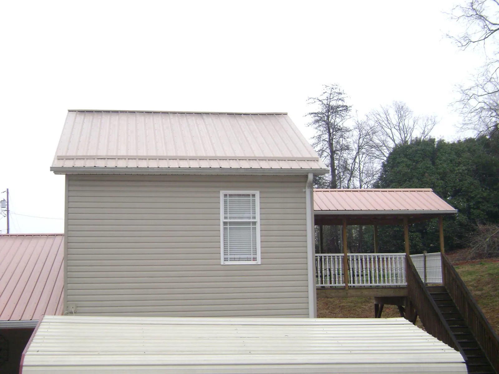 Tan metal roofs on a two story addition and attached porch, from a Roof Replacement job in Sevier